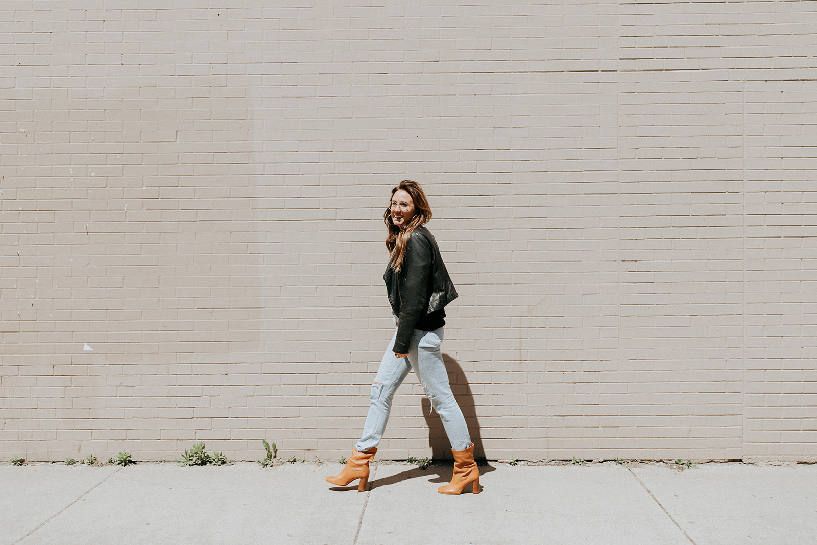 Emily walking beside a sunlit brick wall